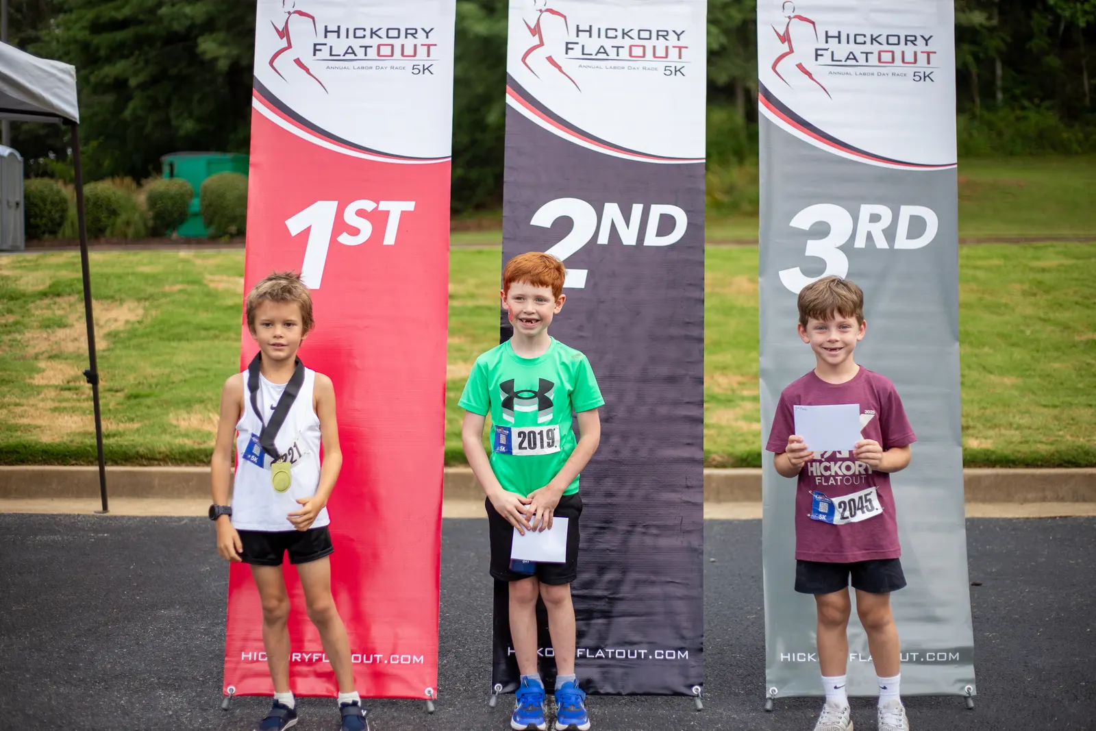Three kids standing in front of the 1st, 2nd and 3rd place banners